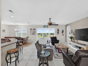 A spacious living area with a dining table, seating, a TV, and a view through the glass doors. - Sunset to Magic 6BR Davenport Home with Private Pool Near Disney (Davenport)
