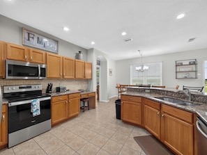 A modern kitchen with wooden cabinets, stainless steel appliances, and a granite countertop. - Sunset to Magic 6BR Davenport Home with Private Pool Near Disney (Davenport)