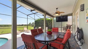 Eine überdachte Terrasse im Freien mit einem runden Tisch und Stühlen, einem Deckenventilator und einem an der Wand befestigten Fernseher.