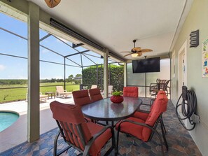 A covered outdoor patio with a round table and chairs, a ceiling fan, and a TV mounted on the wall. - Sunset to Magic 6BR Davenport Home with Private Pool Near Disney (Davenport)