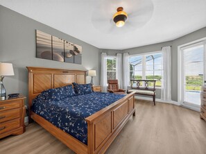 A bedroom with a large bed, a wooden headboard, a nightstand, a chair, and a view of the outdoors through large windows. - Sunset to Magic 6BR Davenport Home with Private Pool Near Disney (Davenport)