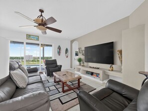 Ein modernes Wohnzimmer mit Ledersofas, einem Couchtisch, einem Fernseher und einem Deckenventilator.