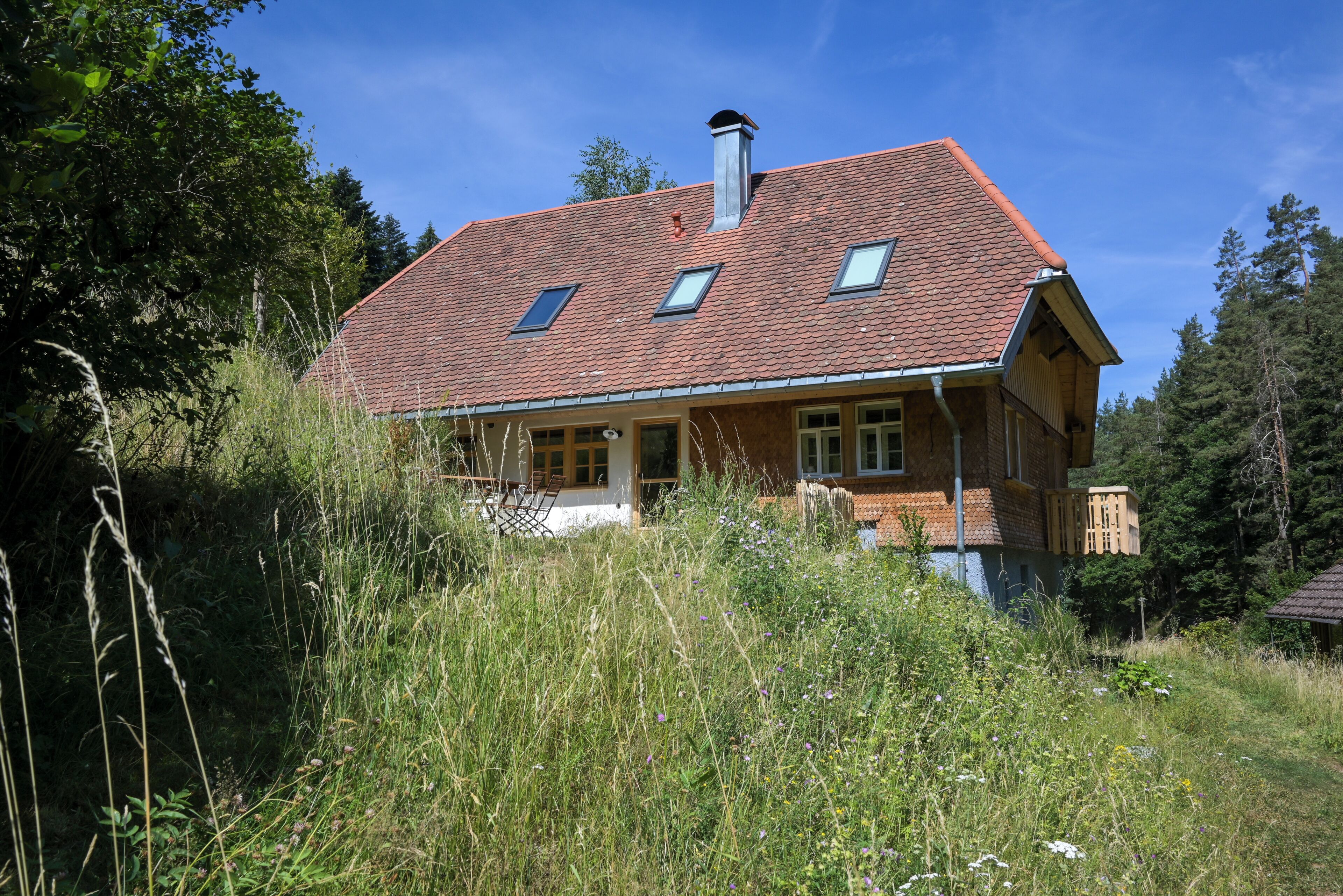 A two-story house with a red-tiled roof, a chimney, and a balcony.