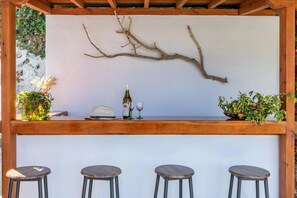Eine Bar mit einer Holztheke, einer Weinflasche, zwei Gläsern und drei Barhocker.