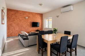 A modern living room with a sofa, a dining table with chairs, a flat-screen TV mounted on the wall, and an air conditioning unit. - Villa Odzakovic - Four Bedroom Villa, Sleeps 8 (Nadin)