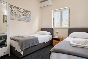 A hotel room with two beds, a bedside table, a lamp, a window with blinds, and a wall-mounted air conditioner. - Villa Odzakovic - Four Bedroom Villa, Sleeps 8 (Nadin)