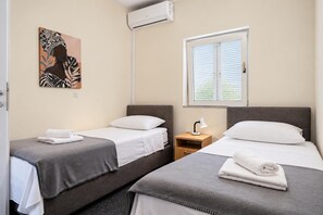 A hotel room with two single beds, a nightstand with a lamp, a window with blinds, and a wall-mounted air conditioner. - Villa Odzakovic - Four Bedroom Villa, Sleeps 8 (Nadin)