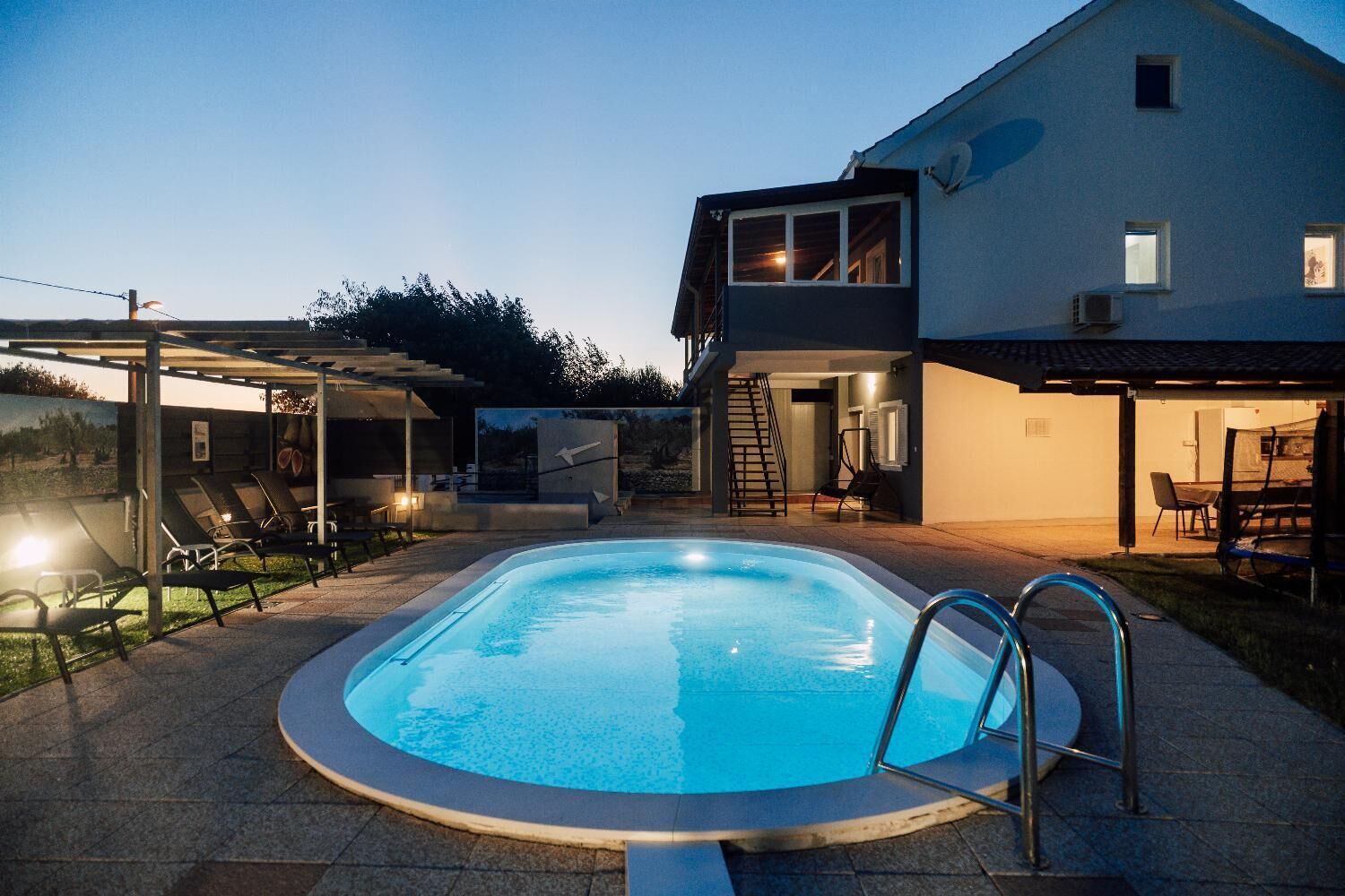 A swimming pool with a sunken deck, surrounded by lounge chairs and a covered seating area.