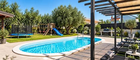 Private swimming pool with sun loungers, pergola shade, mature trees, and a relaxing landscaped garden.