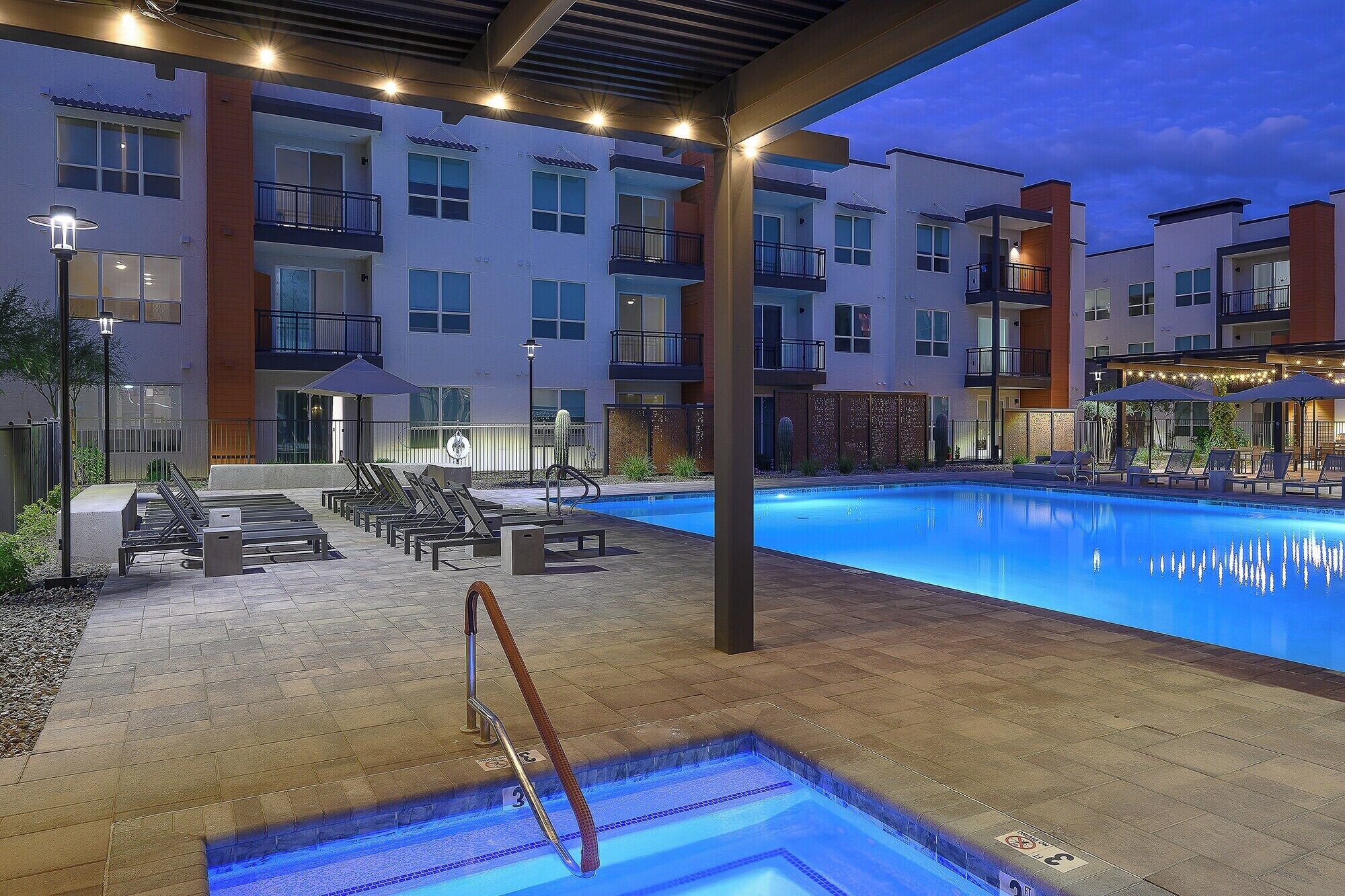 A swimming pool area with lounge chairs and a pool deck, surrounded by multi-story buildings with balconies.