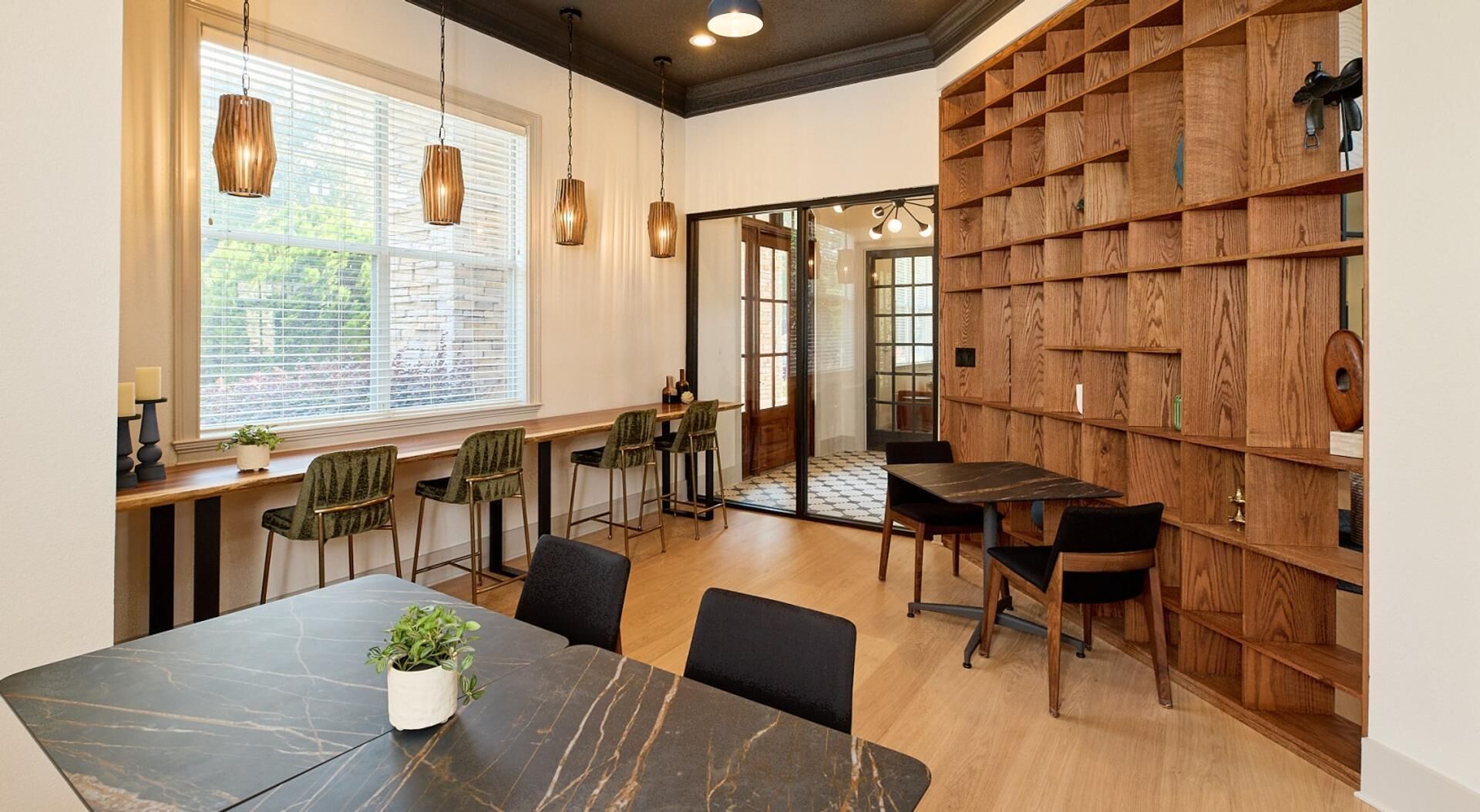 A modern dining area with a marble table, green upholstered chairs, and a wooden bookshelf.