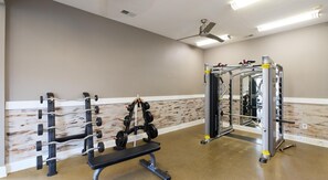 Una sala de gimnàstica amb equips de musculació, una banca i un mirall gran.