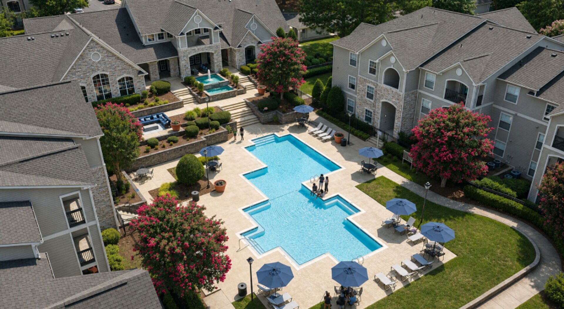 A residential area with a central swimming pool surrounded by lounge chairs and umbrellas, with houses in the background.