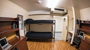 A dormitory room with bunk beds, a desk with a laptop, a trash bin, and a poster on the wall. - Danna apartment  (Crested Butte)