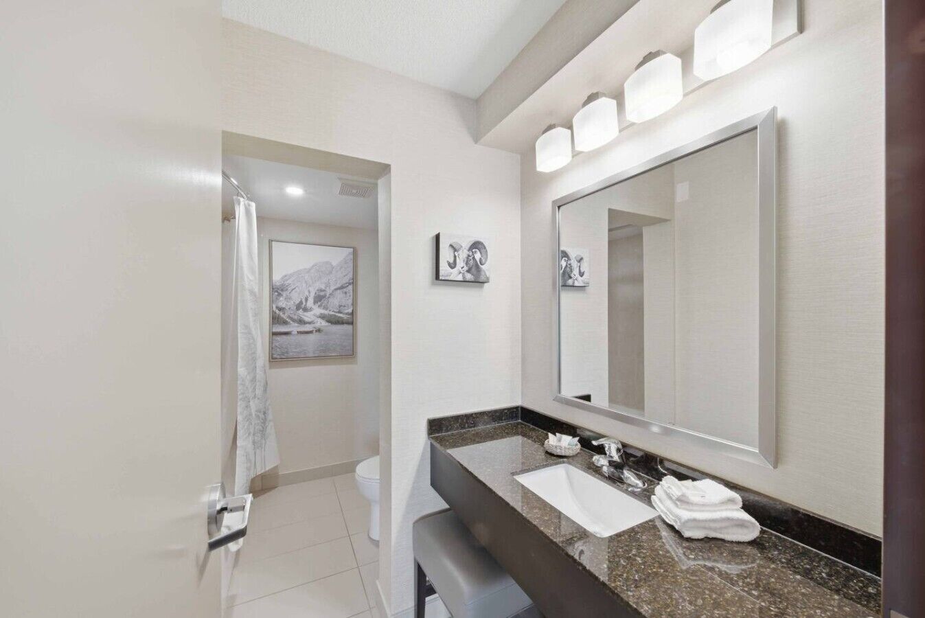 A modern bathroom with a large mirror, a sink, and a toilet. There are framed pictures on the wall and a towel on the counter.