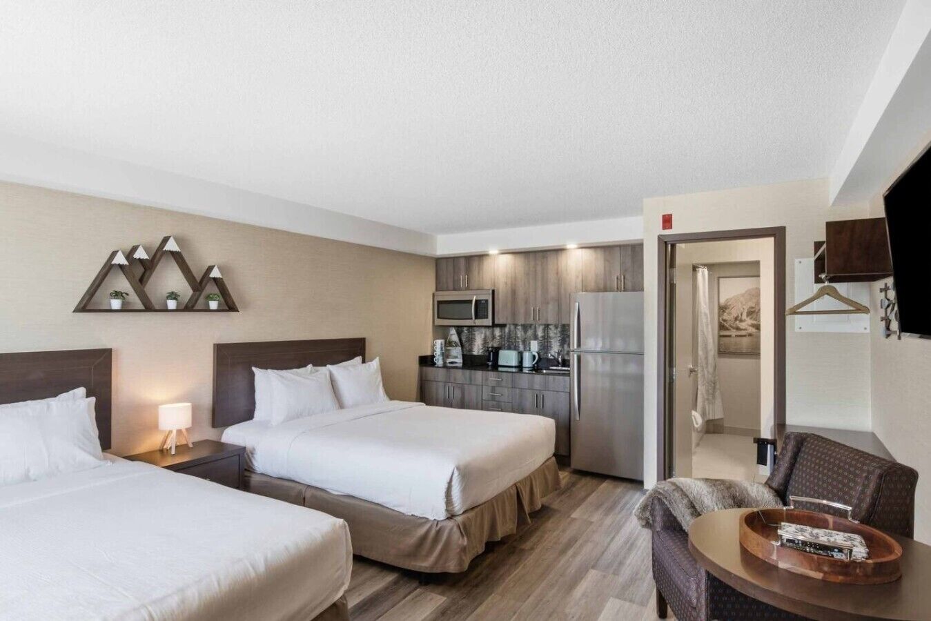 A hotel room with two beds, a kitchenette, a TV, and a seating area with a table.