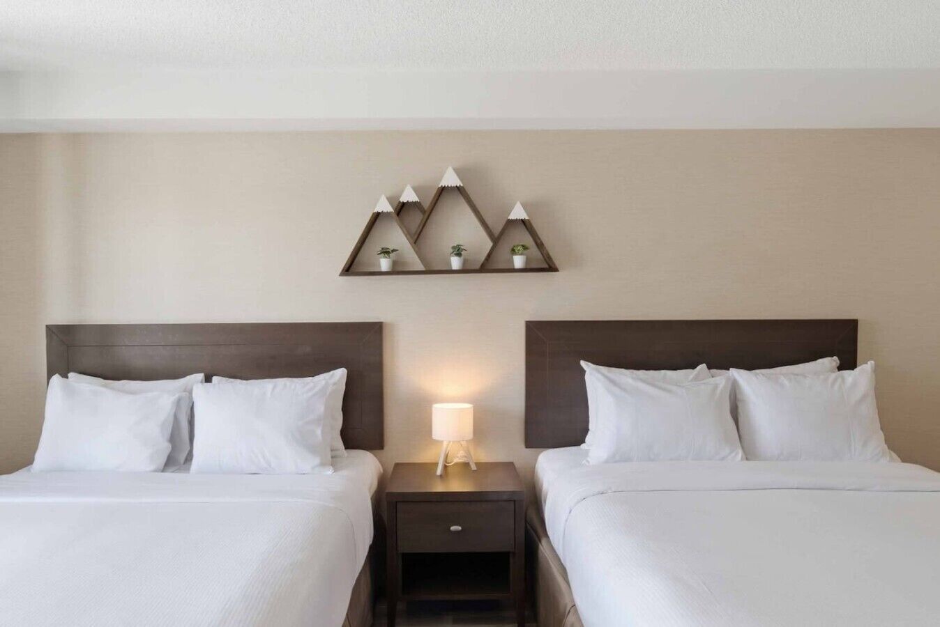 Une chambre d’hôtel avec deux lits, une table de chevet avec une lampe et une étagère murale agrémentée d’objets décoratifs.