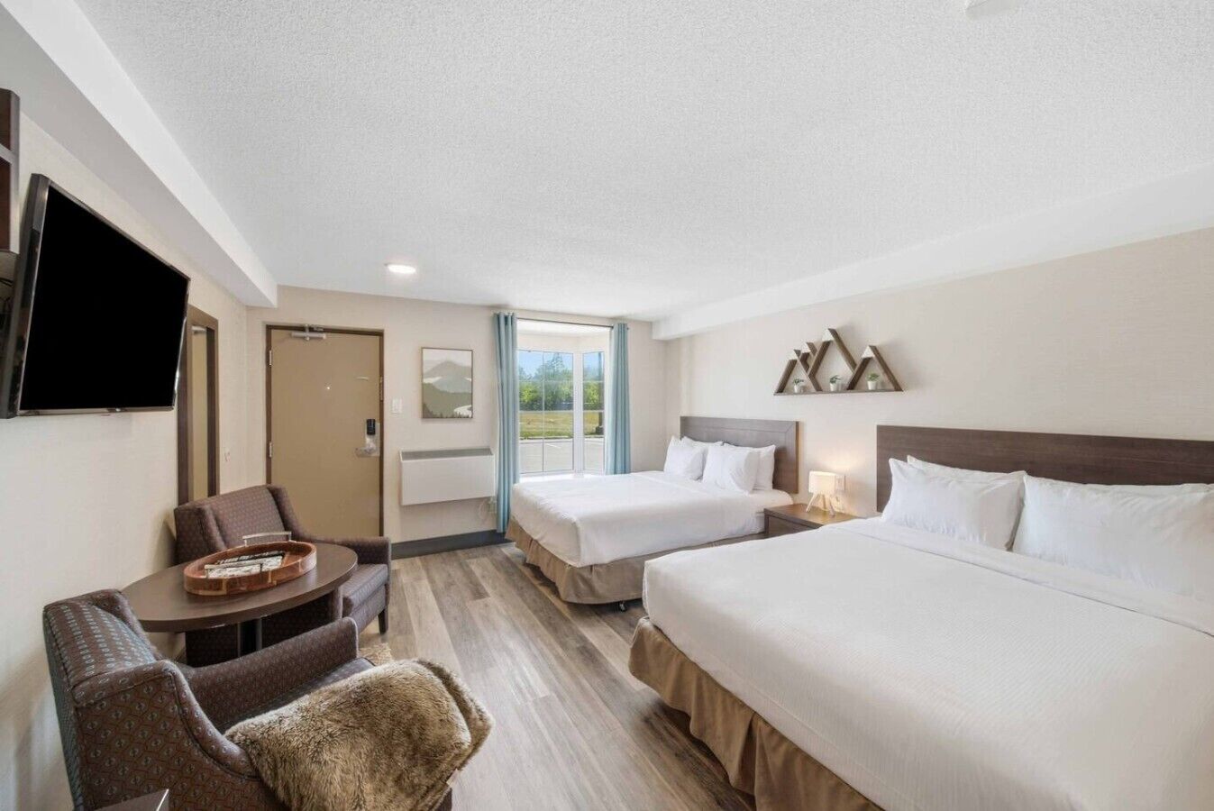 A hotel room with two beds, a desk, a chair, a TV, and a window with a view.