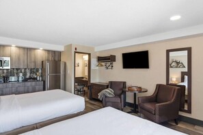 Una habitación de hotel con dos camas, kitchenette, televisión y zona de estar.