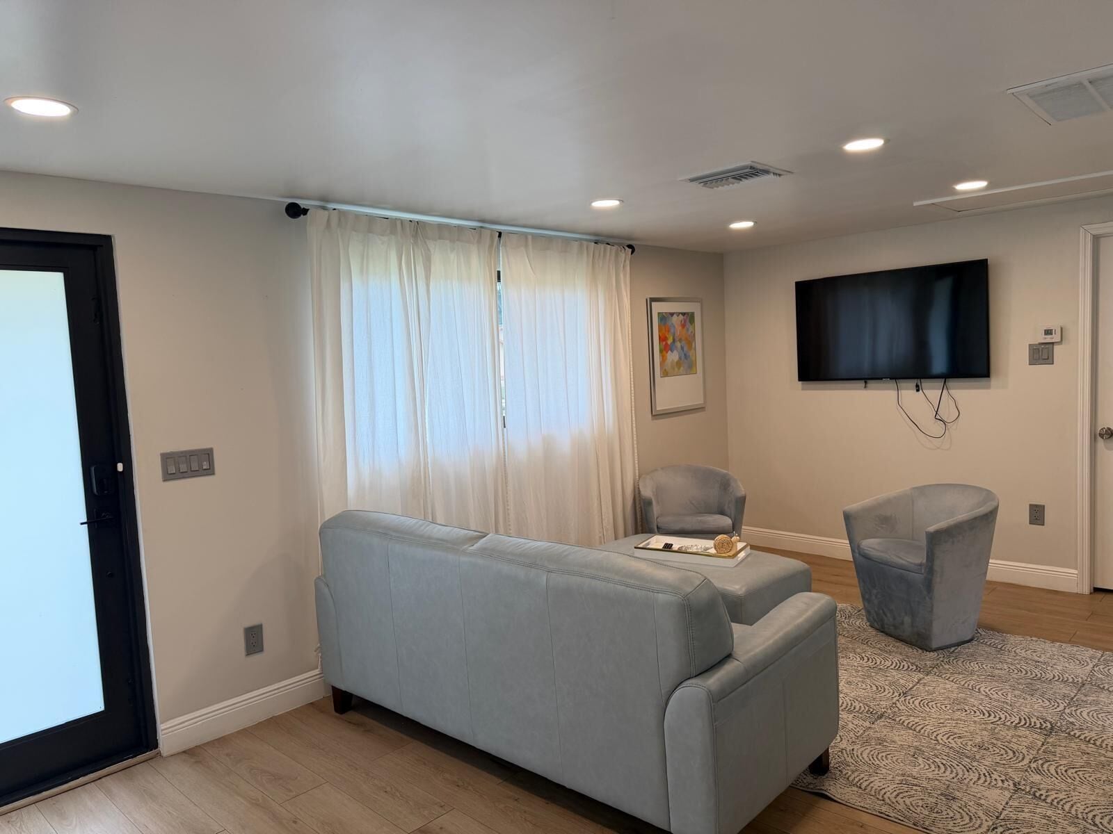Una sala de estar moderna con un sofá, un sillón, un televisor de pantalla plana y una alfombra estampada.