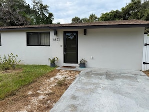 Uma casa térrea com porta da frente preta, um pequeno alpendre e o número '8835' na parede.