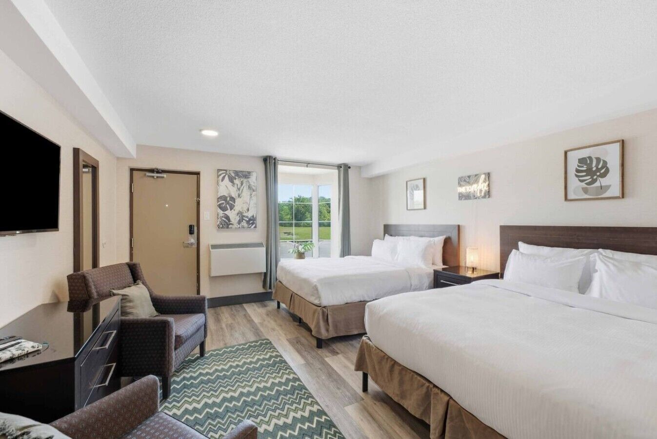 A hotel room with two beds, a desk, a chair, a flat-screen TV, and artwork on the walls.