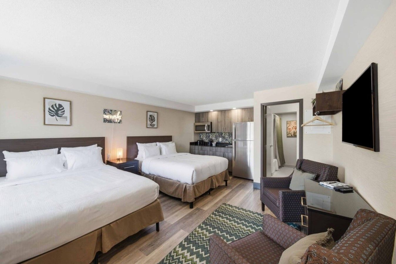 A hotel room with two beds, a kitchenette, a seating area, and a TV.