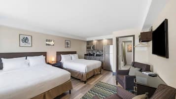A hotel room with two beds, a kitchenette, a seating area, and a TV.