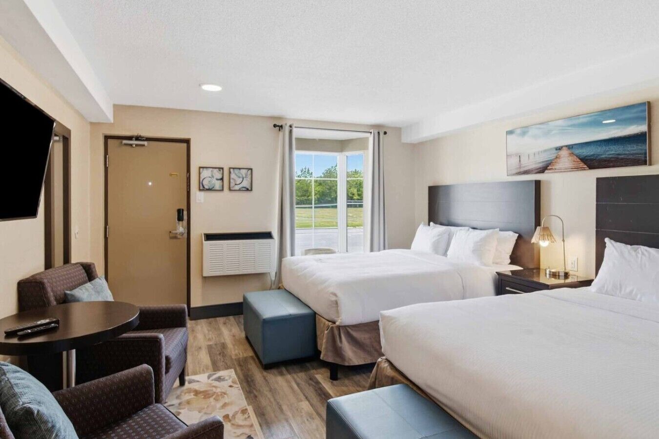 Une chambre d’hôtel avec deux lits, un bureau, une chaise, une télévision et une grande fenêtre donnant sur un paysage verdoyant.