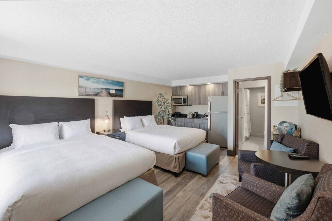 Une chambre d’hôtel avec deux lits, une kitchenette, un coin salon avec une table et un téléviseur fixé au mur.