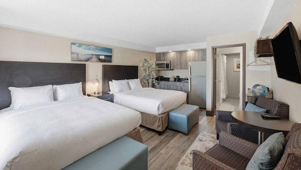 Een hotelkamer met twee bedden, een kitchenette, een zithoek met een tafel en een aan de muur bevestigde televisie.