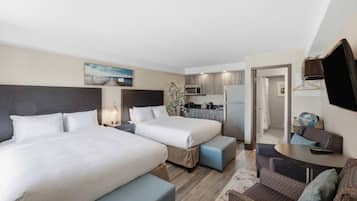 Une chambre d’hôtel avec deux lits, une kitchenette, un coin salon avec une table et un téléviseur fixé au mur.
