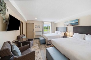 Habitación de hotel con una cama, dos mesitas de noche, un televisor, una zona de estar con un sofá y sillas, y una ventana con vistas.