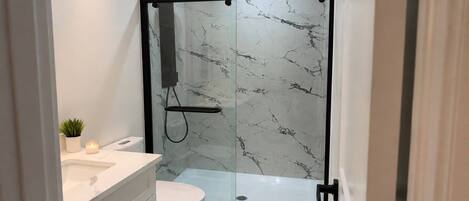 Un baño moderno con ducha envuelta en vidrio, inodoro blanco y tocador con cajones.