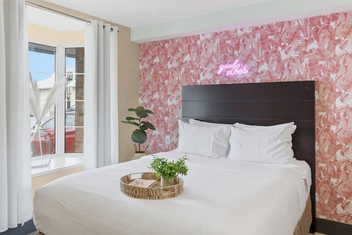 A hotel room with a bed, a neon sign, a window with curtains, and a balcony.
