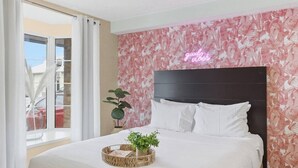Une chambre d’hôtel avec un lit, un panneau lumineux au néon, une fenêtre avec des rideaux et un balcon.