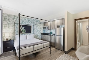 Un dormitorio moderno con cama con dosel, una kitchenette con refrigerador y un baño con cortina de ducha.