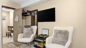 A hotel room with two white armchairs, a small table with a green box, a flat-screen TV, and a mirror on the wall.