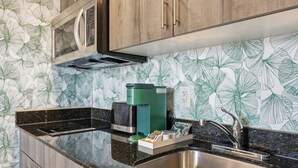 Een keuken met een roestvrijstalen spoelbak, een groene koffiezetapparaat en een aanrecht met een backsplash met bladmotief.