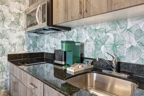 Una cocina con un lavamanos de acero inoxidable, una cafetera verde y una encimera con salpicadero estampado con motivos de hojas.