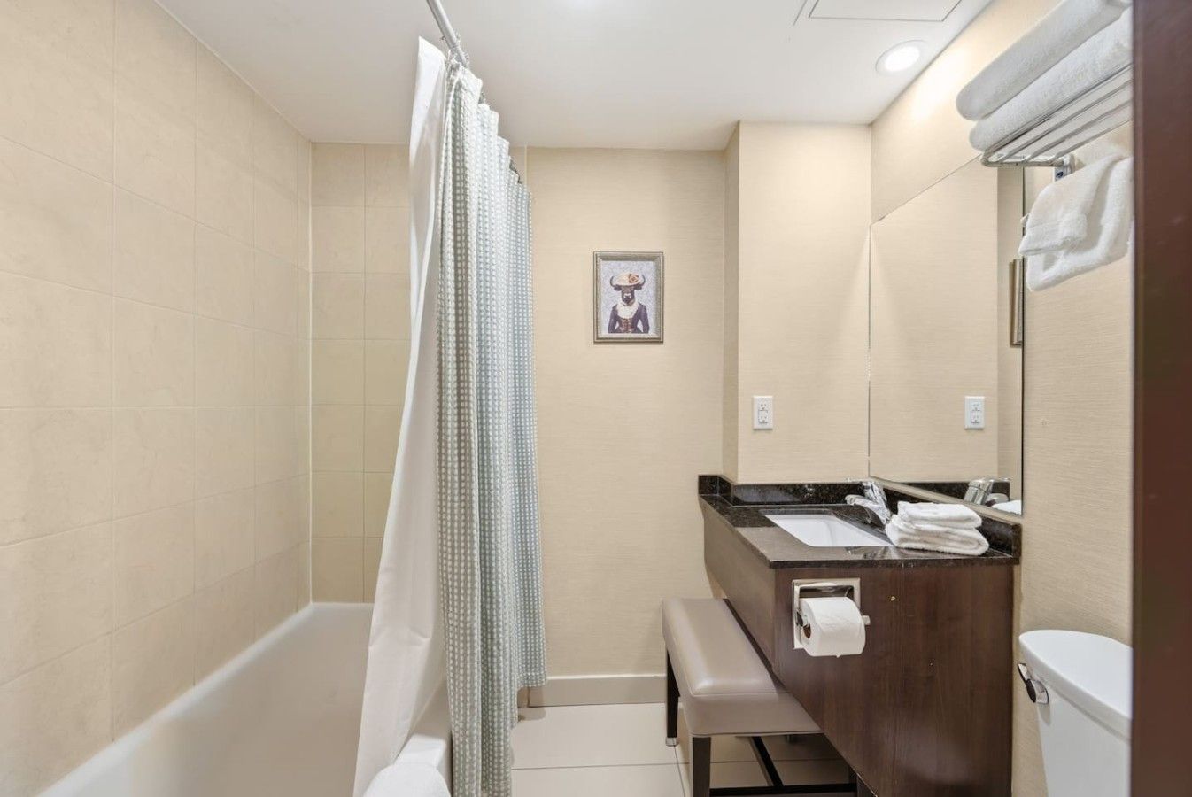 Une salle de bain avec une baignoire, un rideau de douche, un banc, un lavabo avec un miroir et des toilettes.