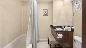 Een badkamer met een bad, douchegordijn, een bankje, een wastafel met spiegel en een toilet.