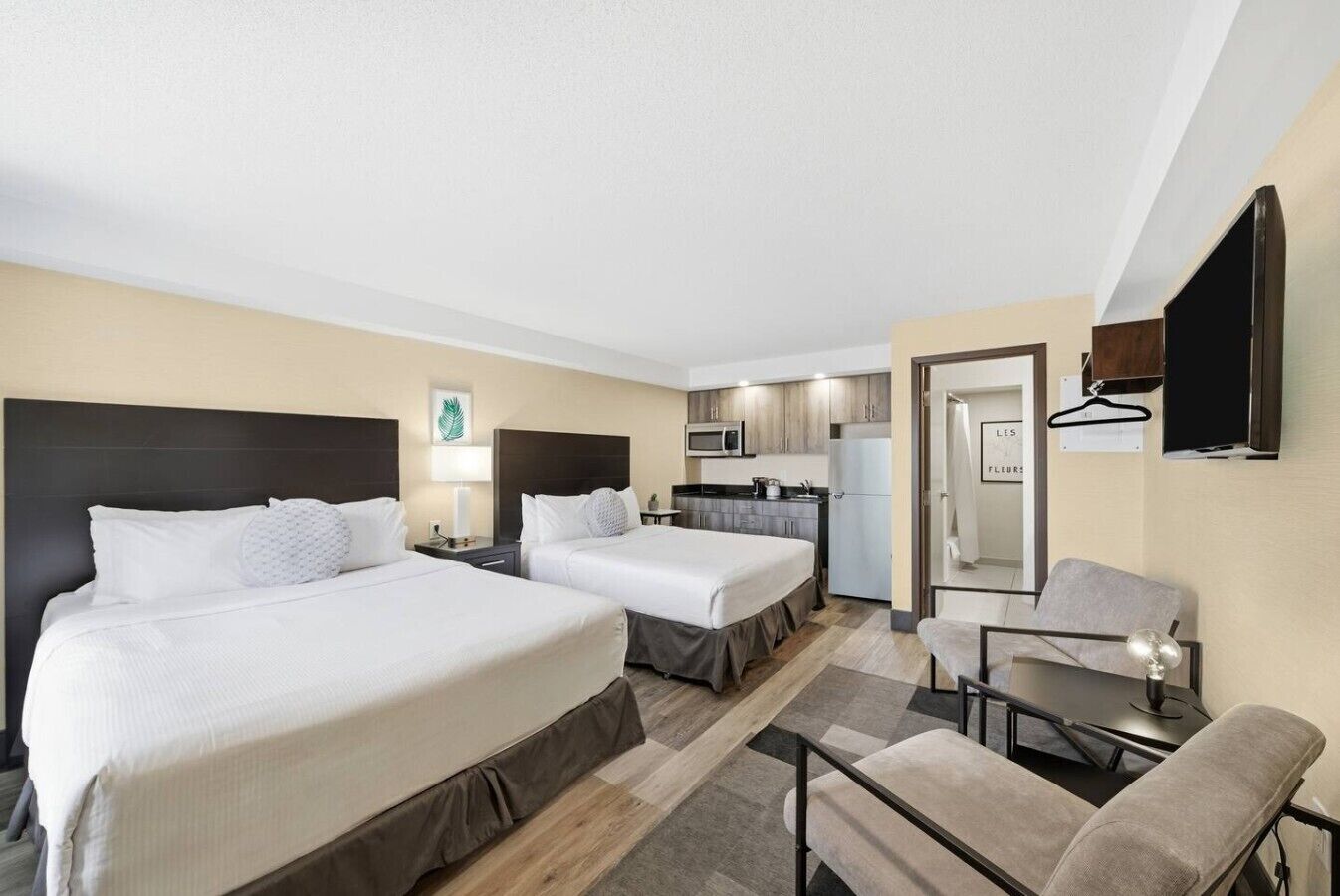 Une chambre d’hôtel avec deux lits, une kitchenette, un petit coin repas et un miroir.
