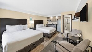 Ein Hotelzimmer mit zwei Betten, einer Küchenzeile, einer kleinen Essecke und einem Spiegel.