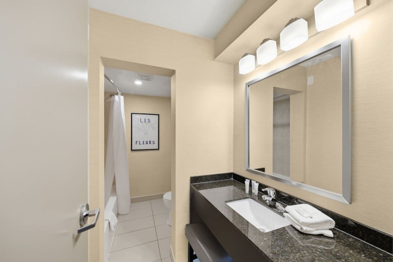 Une salle de bain moderne avec un grand miroir, un lavabo avec une serviette et un espace douche.