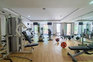 Un gimnasio con diverso equipo de ejercicio, un espejo grande y piso de madera.