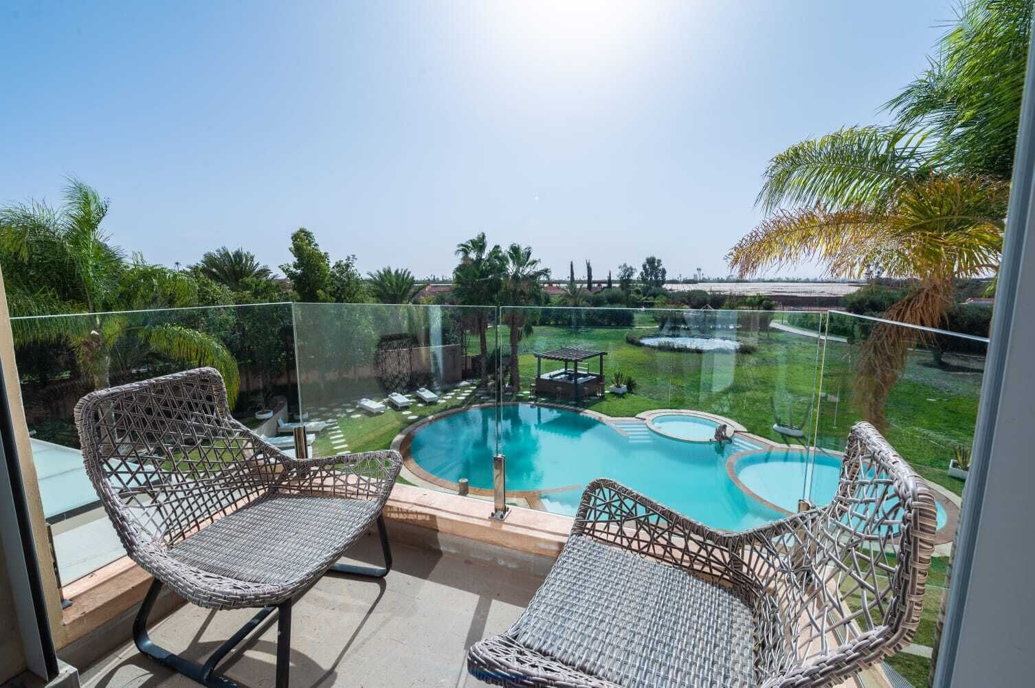 Ein Balkon mit zwei Korbstühlen, einem Schwimmbad und freiem Blick auf die umliegende Bepflanzung.