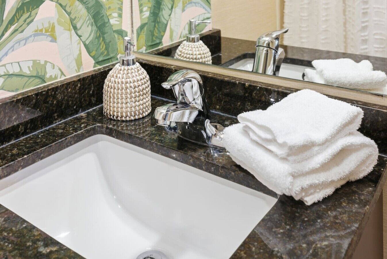 Une salle de bain avec un lavabo blanc, un miroir, une serviette et un distributeur de savon.