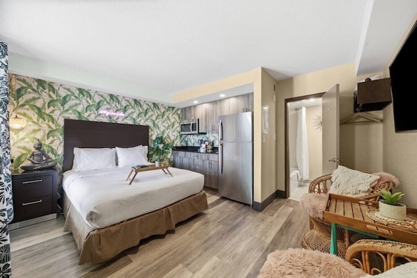 A hotel room with a bed, a small kitchenette, a dining area with a chair, and a bathroom.