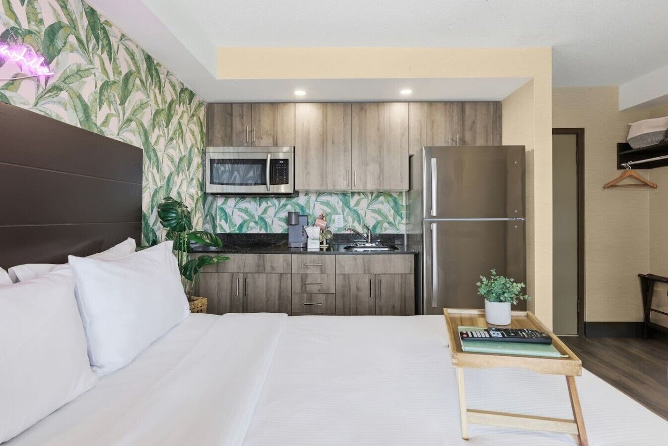Una camera d'albergo con un letto, un angolo cottura, un forno a microonde, un frigorifero e un comodino con una pianta.